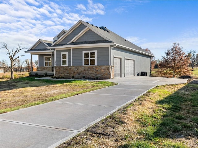 craftsman house featuring stone siding, driveway, an attached garage, and a front lawn