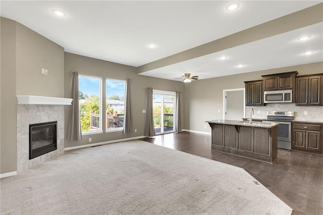 kitchen with baseboards, a premium fireplace, open floor plan, stainless steel range with electric stovetop, and a sink