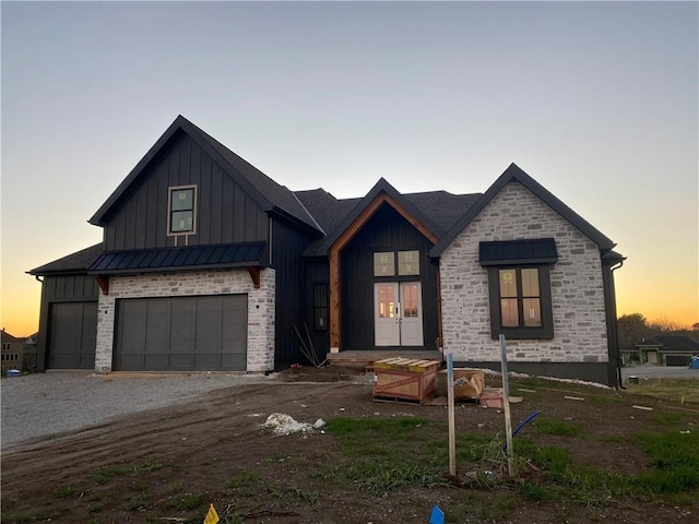 modern inspired farmhouse featuring board and batten siding, gravel driveway, french doors, an attached garage, and a standing seam roof