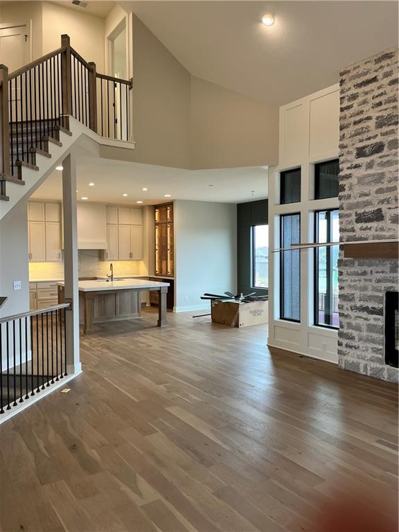 unfurnished living room with wood finished floors, high vaulted ceiling, a fireplace, a sink, and stairs