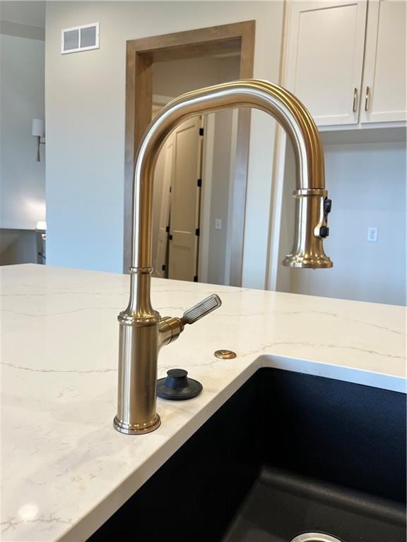 room details featuring visible vents, white cabinetry, and light stone countertops