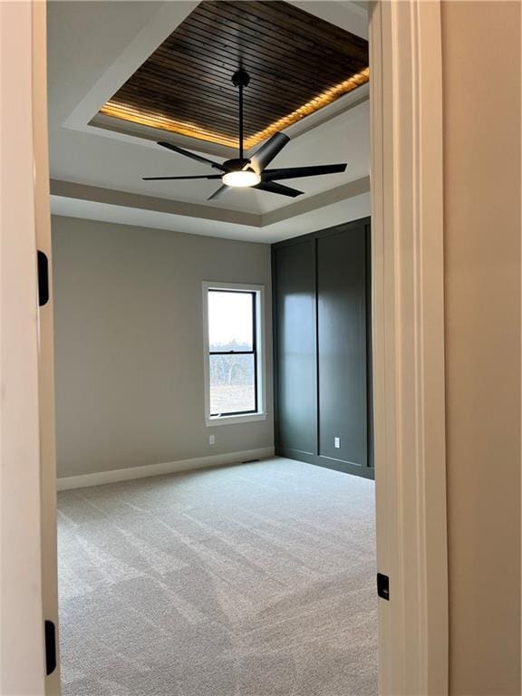 carpeted spare room featuring ceiling fan, a raised ceiling, and baseboards