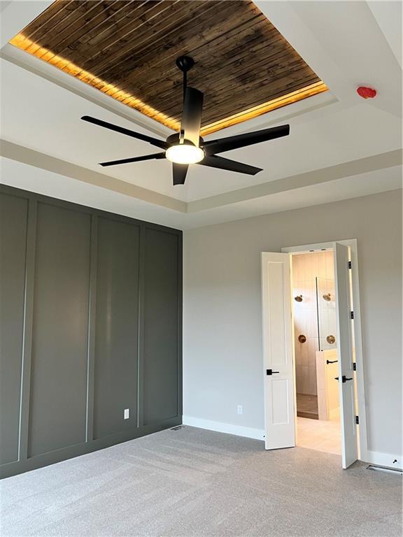 interior space with light carpet, baseboards, wood ceiling, and a tray ceiling