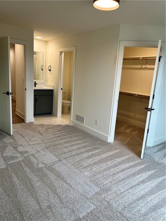 unfurnished bedroom featuring a walk in closet, light colored carpet, visible vents, and baseboards