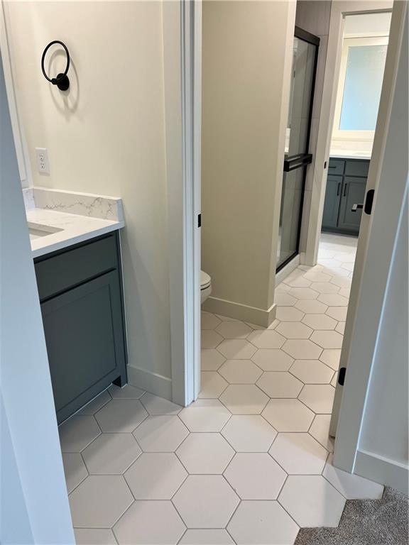 bathroom featuring toilet, a stall shower, vanity, and baseboards