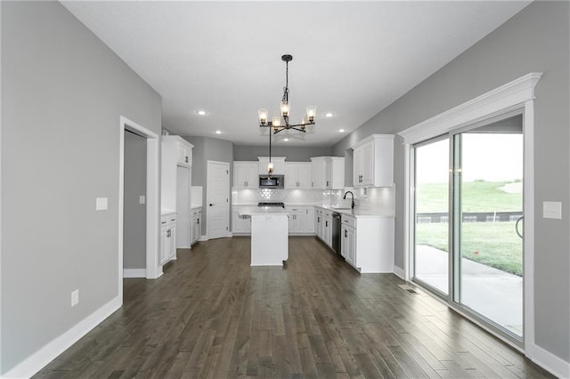 kitchen featuring baseboards, decorative backsplash, a kitchen island, appliances with stainless steel finishes, and dark wood-type flooring