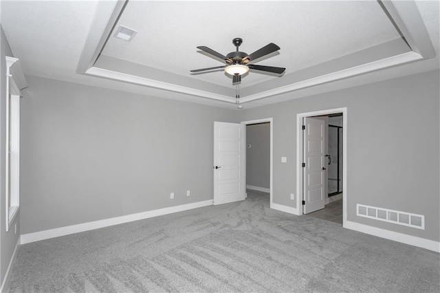 unfurnished bedroom featuring a tray ceiling, carpet, visible vents, and baseboards