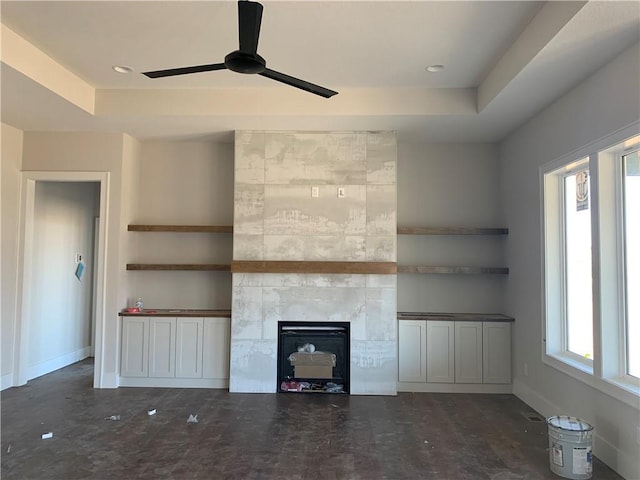 unfurnished living room with ceiling fan, a fireplace, a tray ceiling, and baseboards