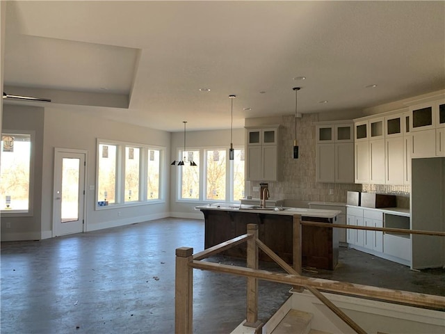 kitchen with a kitchen island with sink, a sink, backsplash, white cabinets, and baseboards