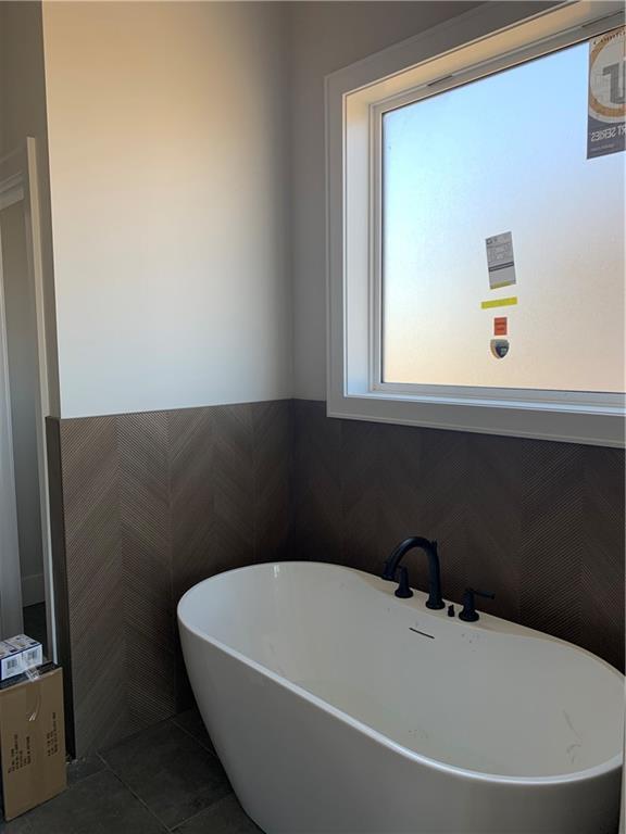 full bathroom with tile patterned floors, a freestanding tub, and a wainscoted wall