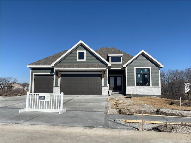 view of front of home with stone siding, driveway, an attached garage, and a shingled roof