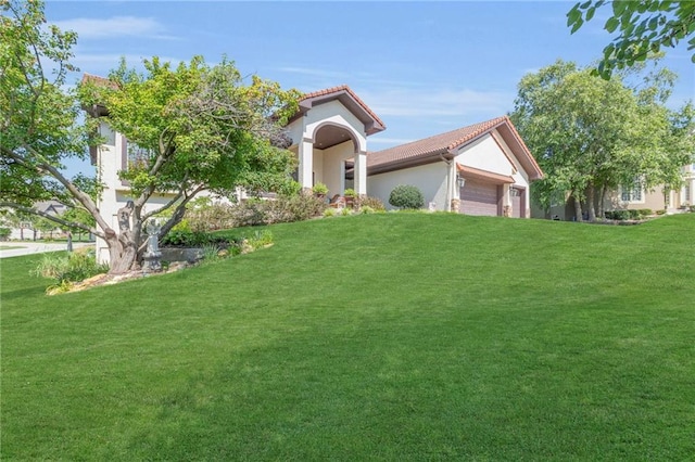 mediterranean / spanish-style home featuring a garage, stucco siding, a front lawn, and a tiled roof