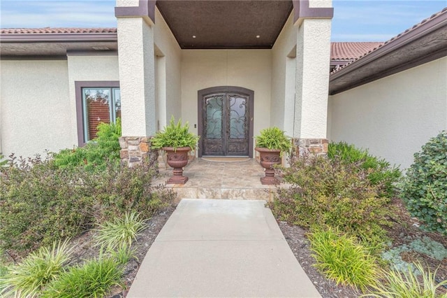 view of exterior entry featuring stone siding, stucco siding, and french doors