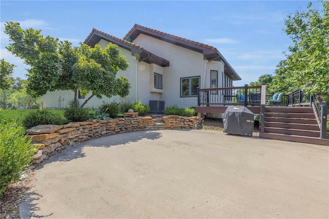 rear view of property with stucco siding, central AC, a wooden deck, and a tile roof