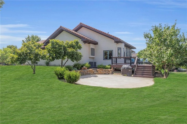 rear view of house featuring central air condition unit, a wooden deck, stucco siding, a lawn, and a patio