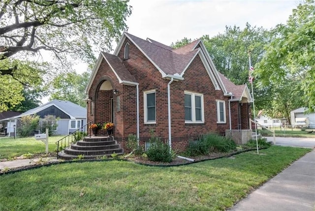 view of front of house with a front yard, brick siding, and roof with shingles