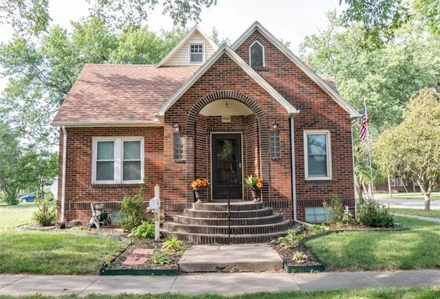 english style home featuring roof with shingles, a front yard, and brick siding