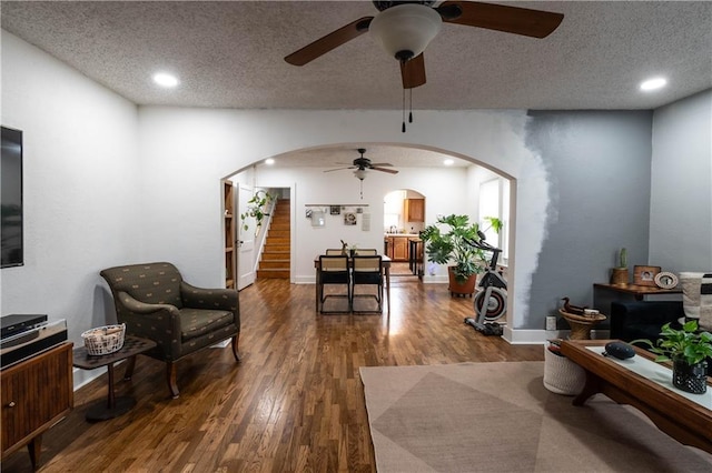 living room with arched walkways, a textured ceiling, wood finished floors, and stairs