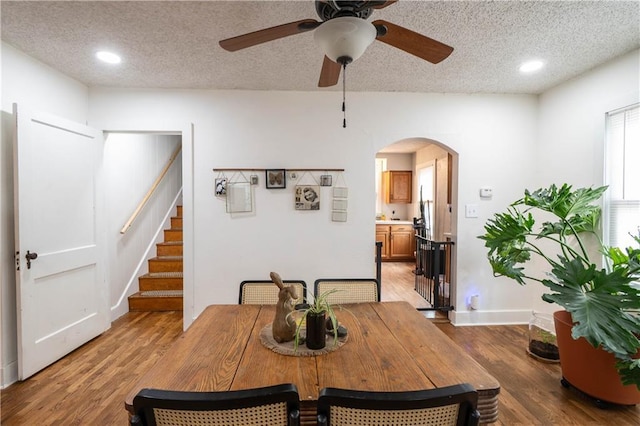 dining space with arched walkways, baseboards, a textured ceiling, and light wood finished floors