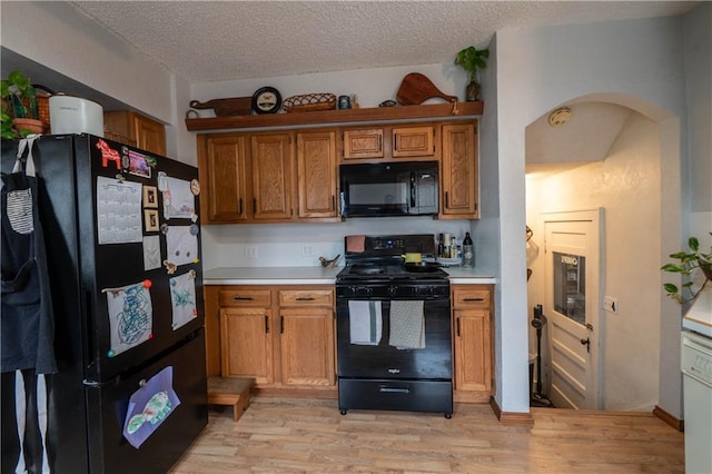 kitchen featuring light wood-type flooring, black appliances, arched walkways, and light countertops