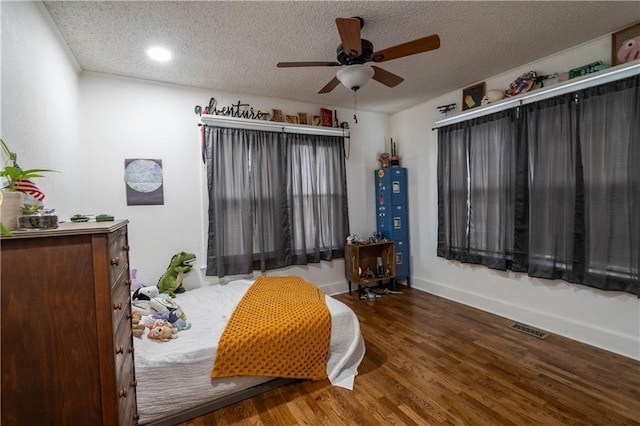 bedroom with a textured ceiling, wood finished floors, visible vents, and baseboards