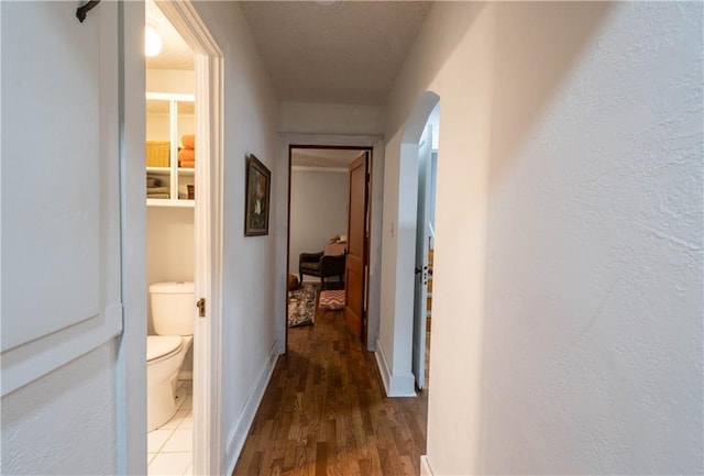 hall with arched walkways, a textured wall, wood finished floors, and baseboards