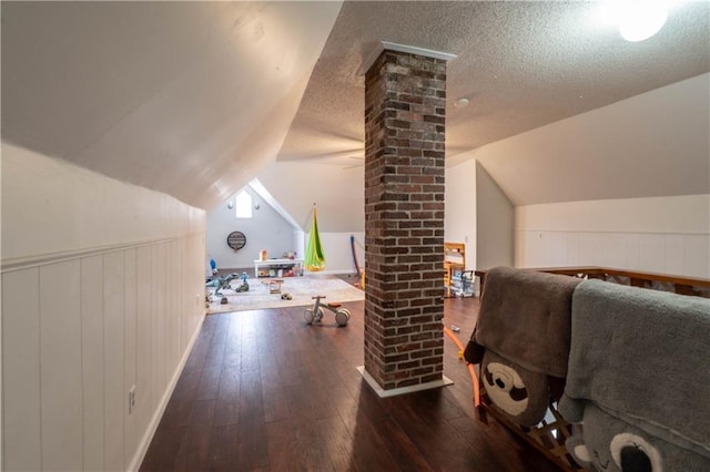 additional living space featuring wainscoting, a textured ceiling, ornate columns, and hardwood / wood-style flooring