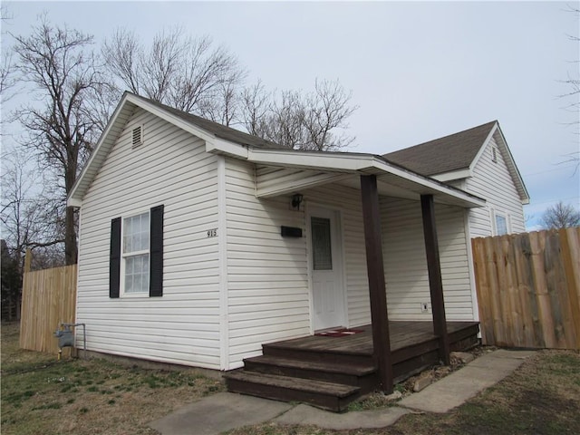 view of front facade with a porch, roof with shingles, and fence