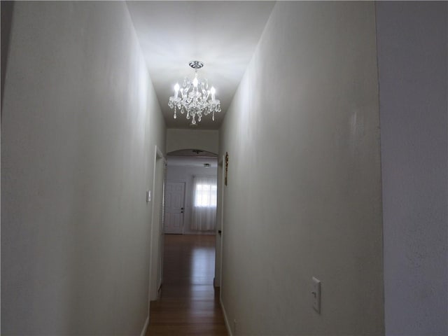 hallway with dark wood-style floors, arched walkways, and an inviting chandelier