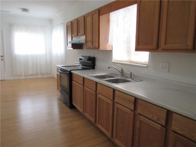 kitchen with brown cabinetry, black / electric stove, light countertops, under cabinet range hood, and a sink