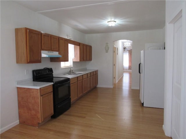 kitchen with arched walkways, freestanding refrigerator, a sink, under cabinet range hood, and black / electric stove