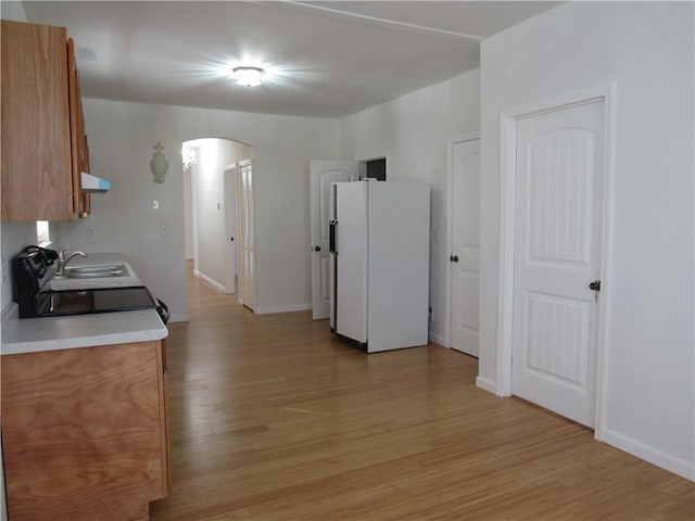 kitchen featuring arched walkways, a sink, exhaust hood, freestanding refrigerator, and light wood finished floors