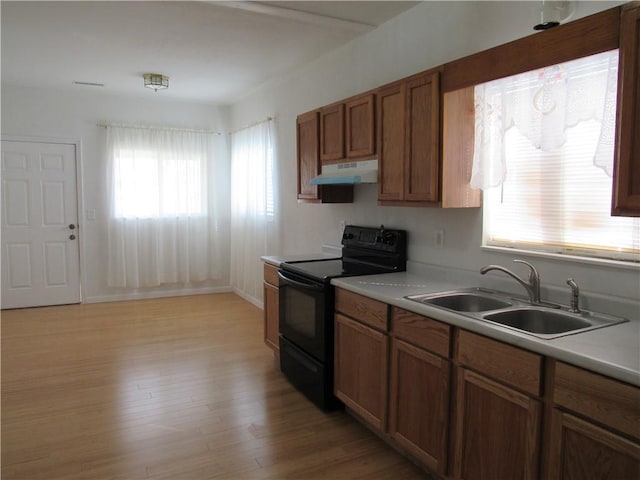 kitchen with light countertops, light wood-style floors, a sink, under cabinet range hood, and black / electric stove