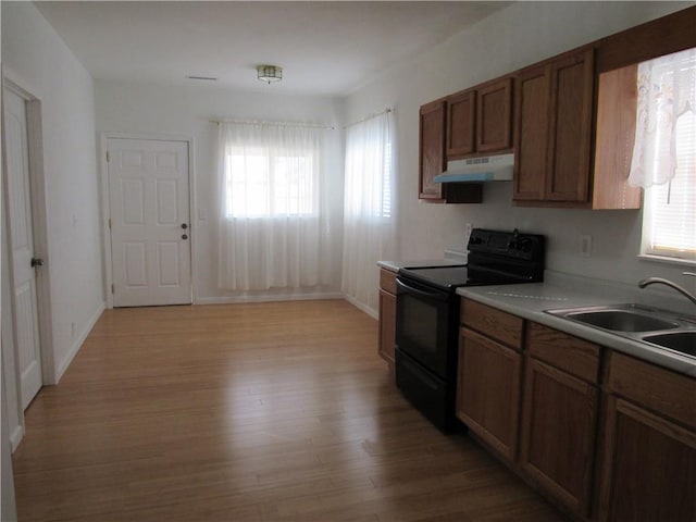 kitchen with black / electric stove, under cabinet range hood, a sink, light wood-style floors, and light countertops