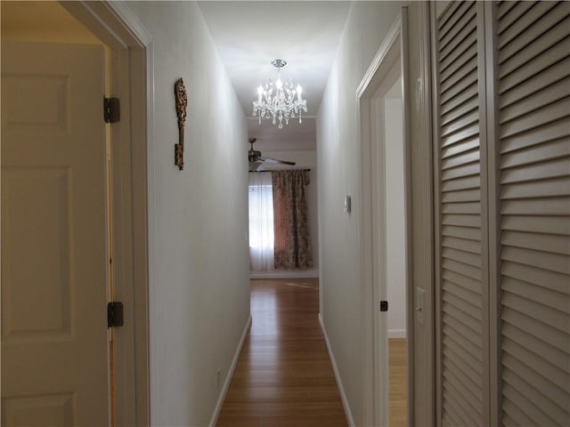 corridor with a chandelier, baseboards, and wood finished floors