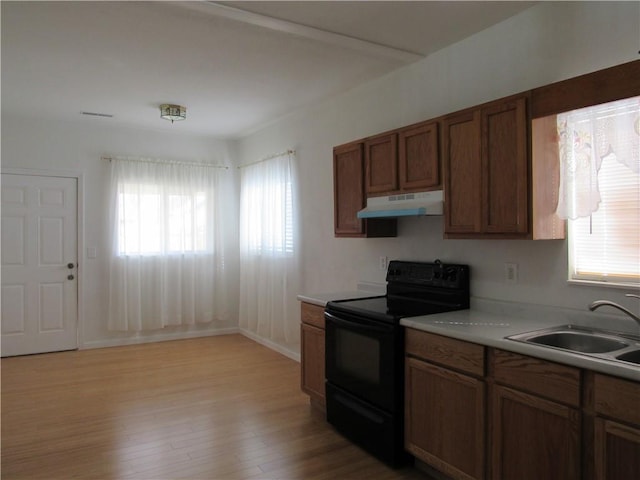 kitchen featuring light wood finished floors, black electric range oven, light countertops, under cabinet range hood, and a sink