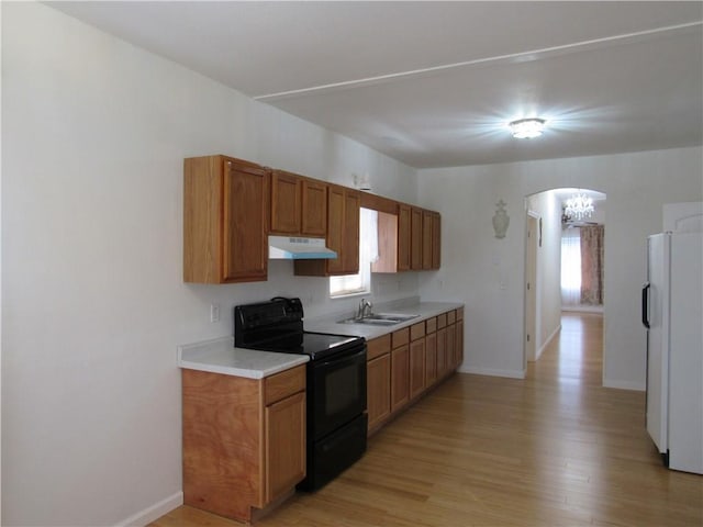 kitchen with arched walkways, freestanding refrigerator, a sink, black range with electric cooktop, and under cabinet range hood