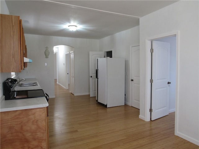 kitchen with arched walkways, extractor fan, freestanding refrigerator, and light wood-style floors