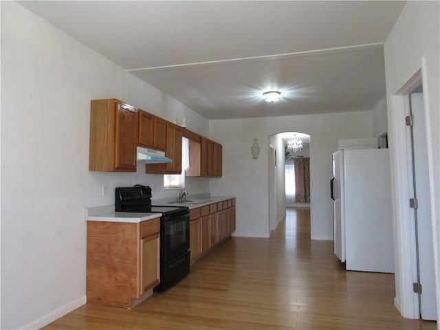 kitchen featuring arched walkways, black / electric stove, under cabinet range hood, a sink, and freestanding refrigerator