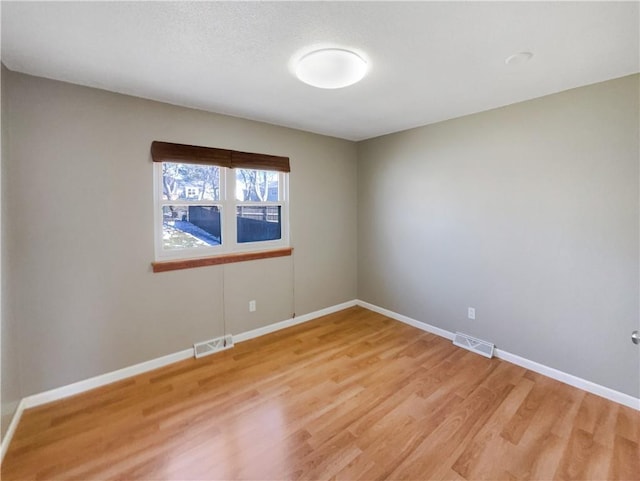 spare room featuring light wood finished floors, baseboards, and visible vents