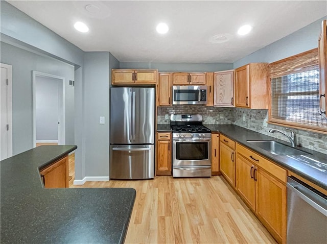 kitchen with dark countertops, backsplash, appliances with stainless steel finishes, a sink, and light wood-type flooring