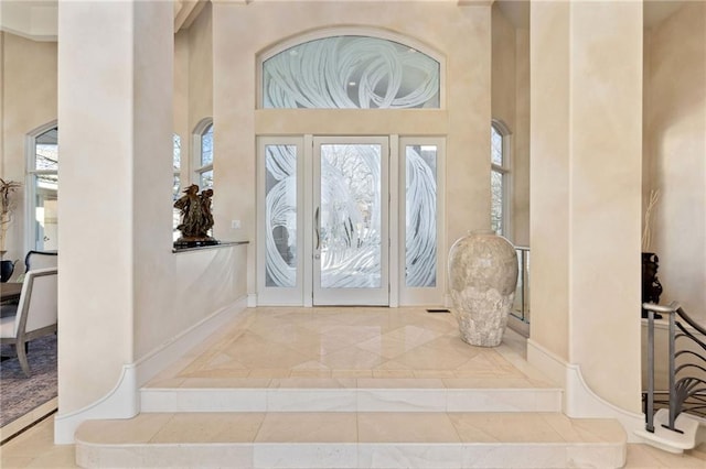 foyer entrance with a towering ceiling, marble finish floor, and baseboards