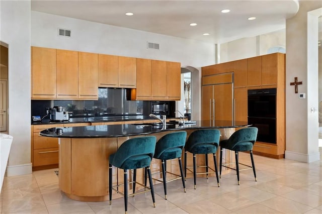 kitchen featuring a large island, dark countertops, visible vents, dobule oven black, and built in refrigerator