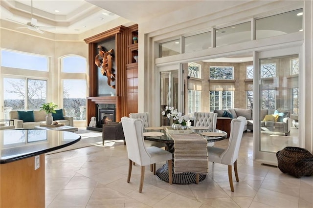 dining space with a ceiling fan, a wealth of natural light, a fireplace, and a high ceiling