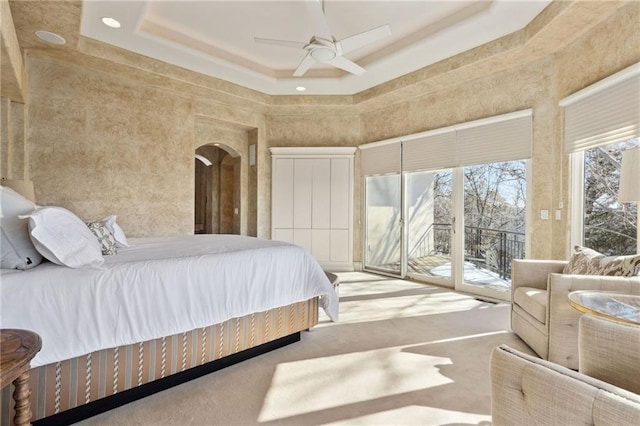 bedroom with ceiling fan, a high ceiling, carpet flooring, access to exterior, and a tray ceiling