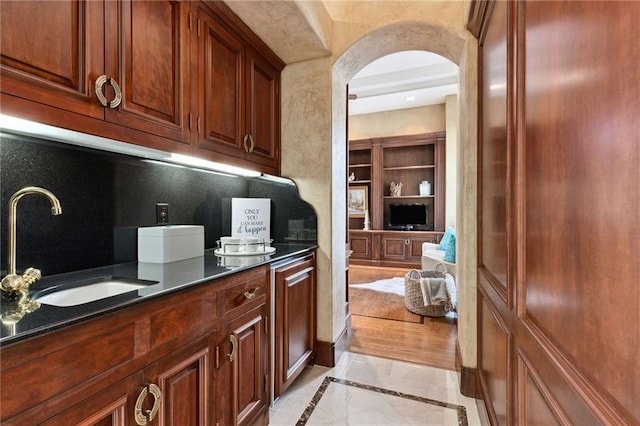 kitchen with dark countertops, arched walkways, a sink, and built in features