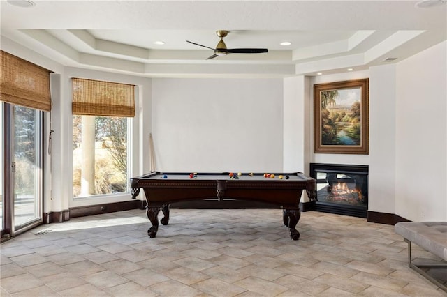 game room featuring a glass covered fireplace, a raised ceiling, ceiling fan, and baseboards