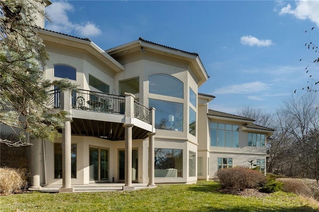 rear view of house featuring a balcony, a lawn, and stucco siding