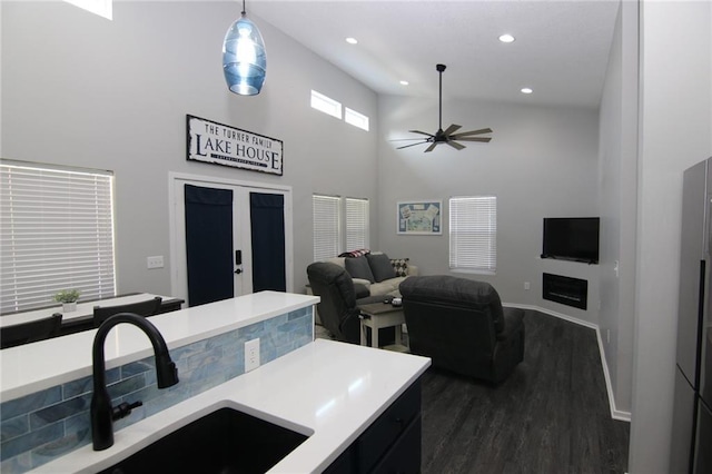 kitchen featuring a ceiling fan, a sink, light countertops, a towering ceiling, and dark wood-style flooring