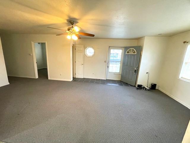 interior space with dark carpet, a wealth of natural light, and baseboards